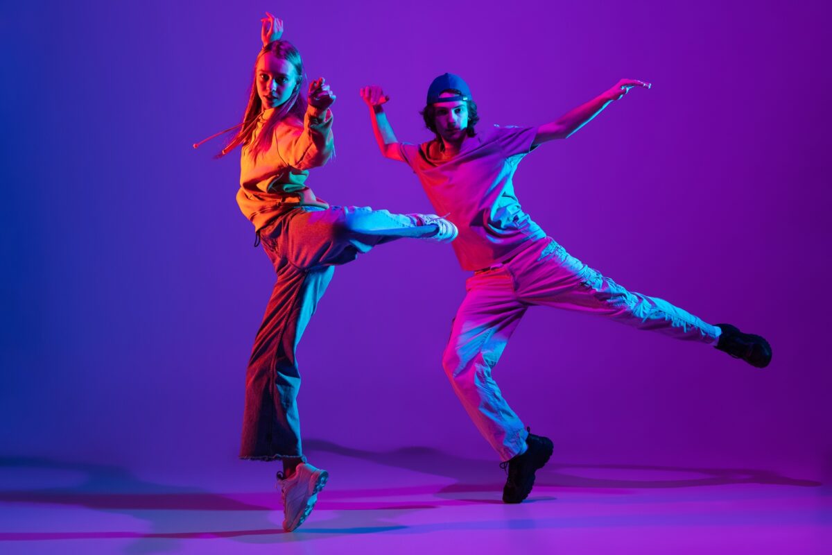 Deux danseurs, un jeune homme et une jeune femme dansant le hip-hop en tenue de sport décontractée sur fond violet dégradé.