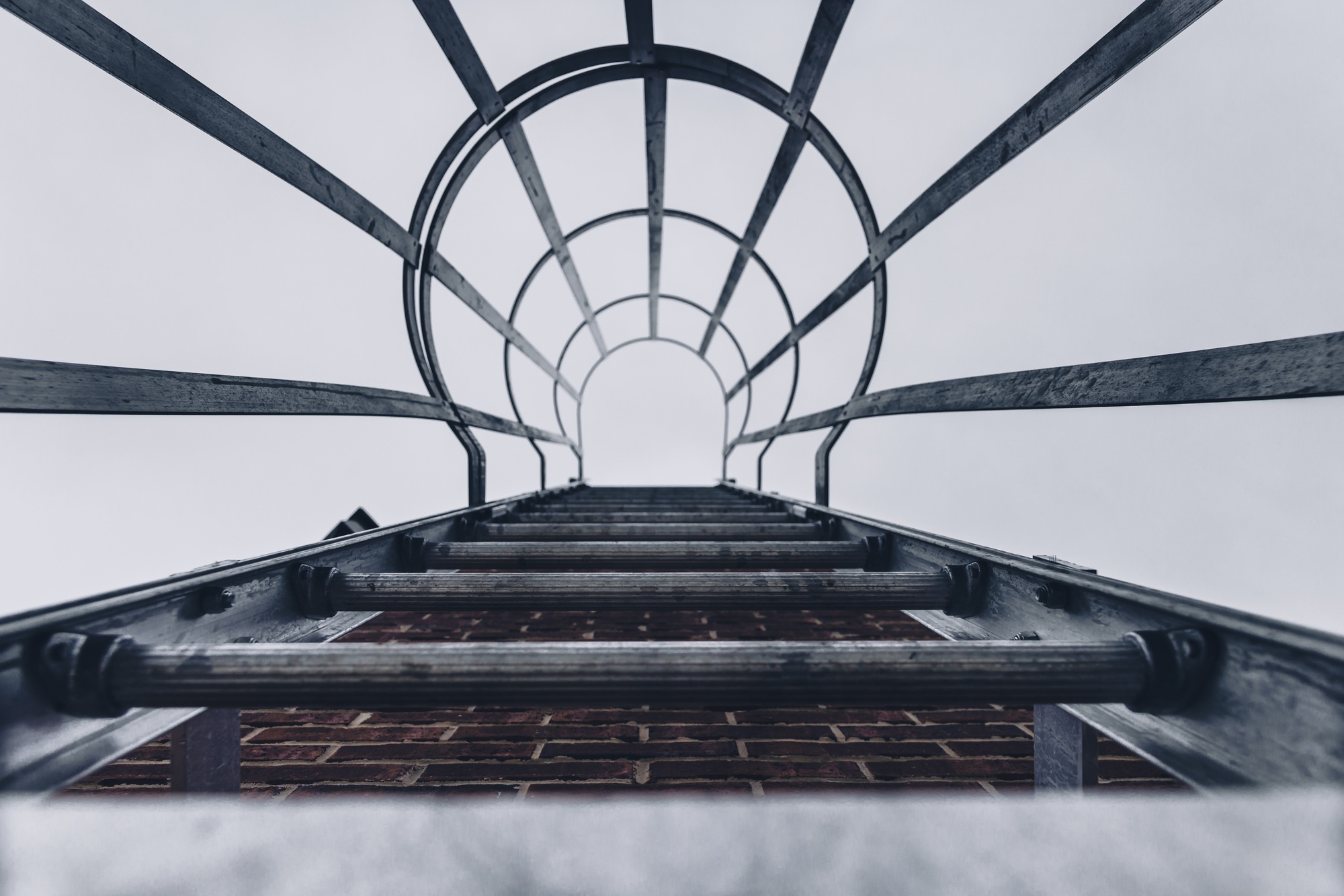 Vue en contre-plongée d'un escalier de secours en métal sur un mur de briques d'un bâtiment avec une cage de sécurité en acier.